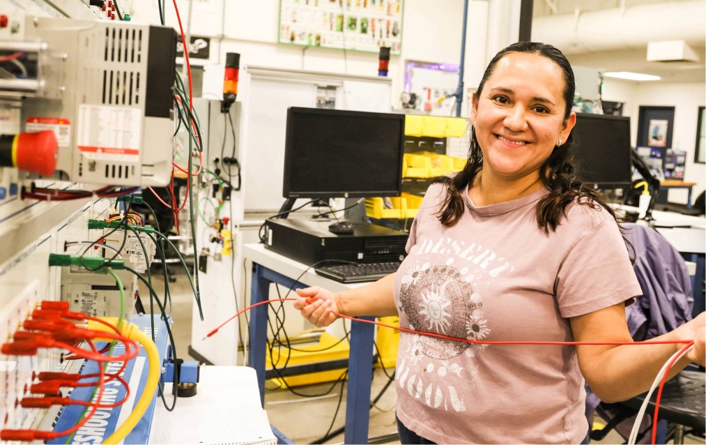A women standing and smiling holding a wire in the manufacturing building at Ogden-Weber Technical College