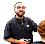 An OTECH Barbering student smiles while performing a haircut on a client, representing the program's hands-on training approach