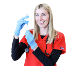 Young woman in red shirt and blue gloves holding a syringe and stethoscope, smiling.