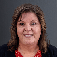 Jennifer Zundel | Ogden-Weber Technical College | Ogden-Weber Technical College Portrait of a smiling woman with shoulder-length brown hair, wearing a red patterned blouse and dark blazer, against a gray background.