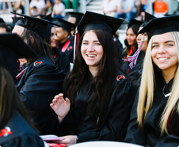 Three young women in black graduation gowns and caps smiling at a ceremony.