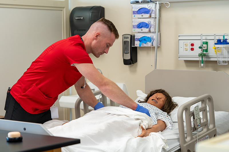 a student practicing skills on a dummy in a hospital bed