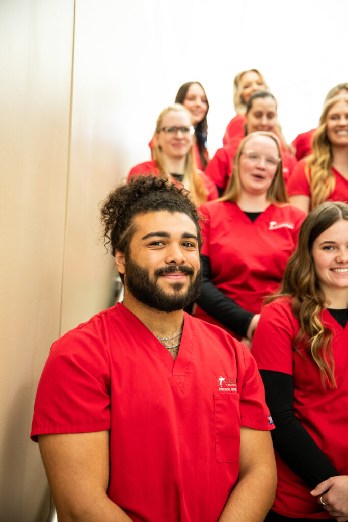Dark haired male practical nursing student stands in front of group of other students.
