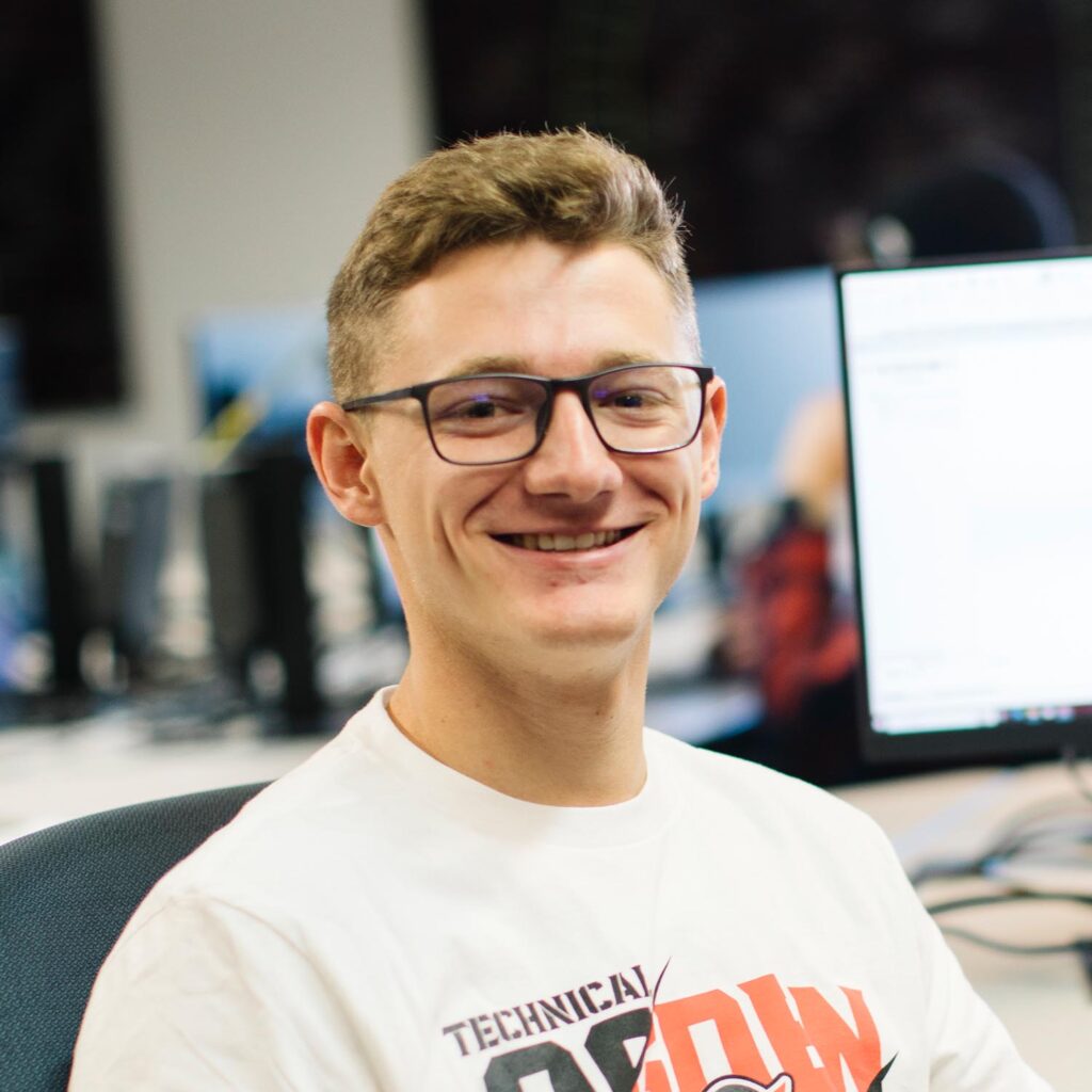 Man smiling with eyes closed in front of computer monitor in office setting.