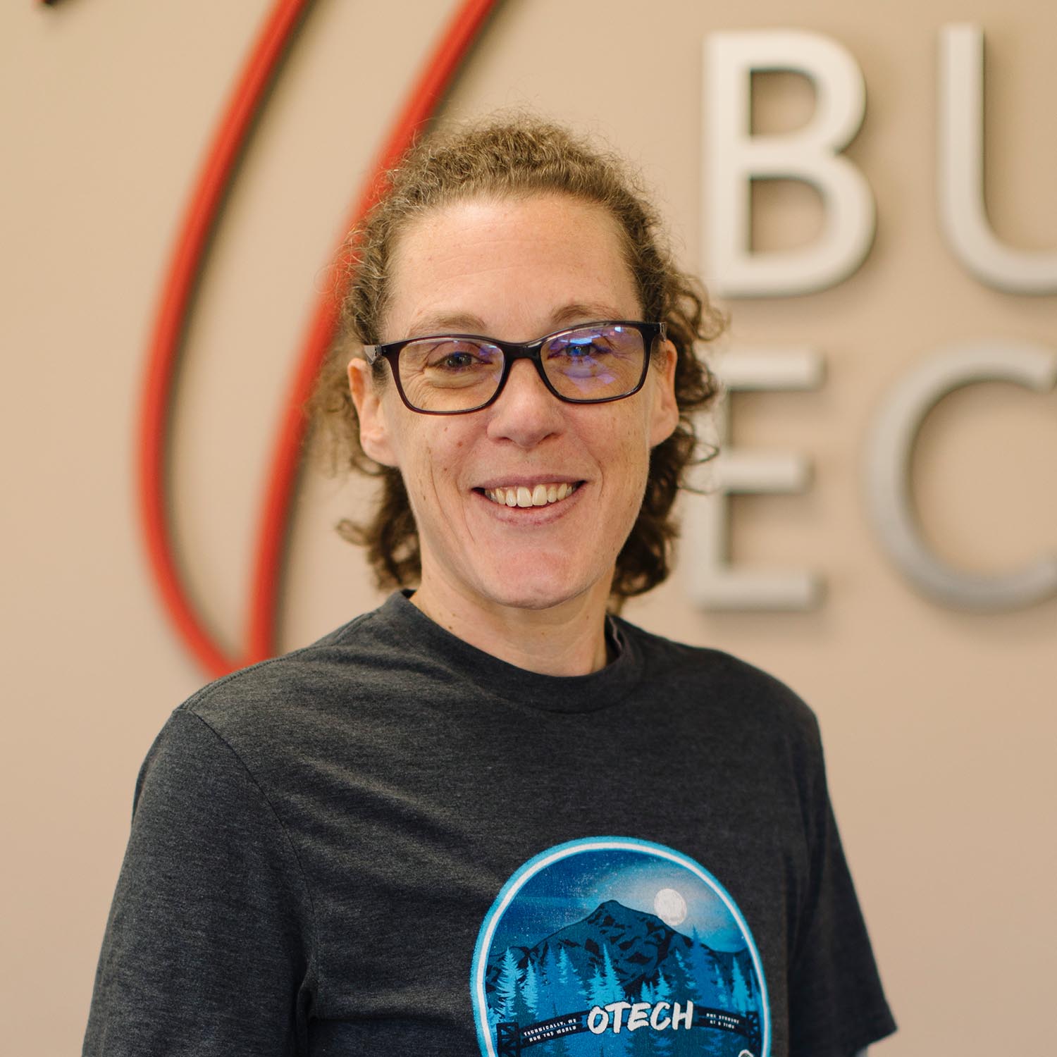 Woman smiling, wearing black t-shirt with blue "BEAR" logo on left.