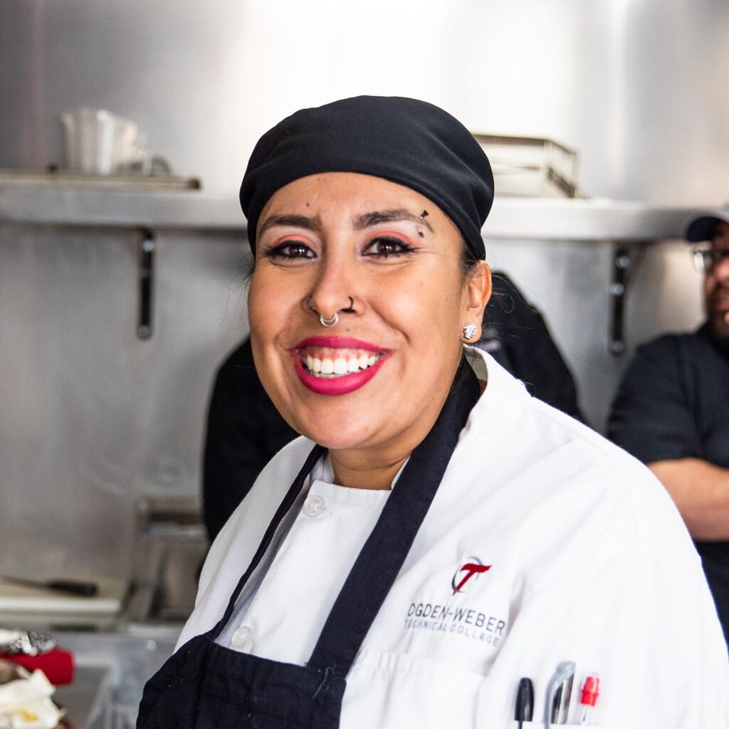 Woman in white chef's apron with logo and name 'Rosa' smiling at the camera.