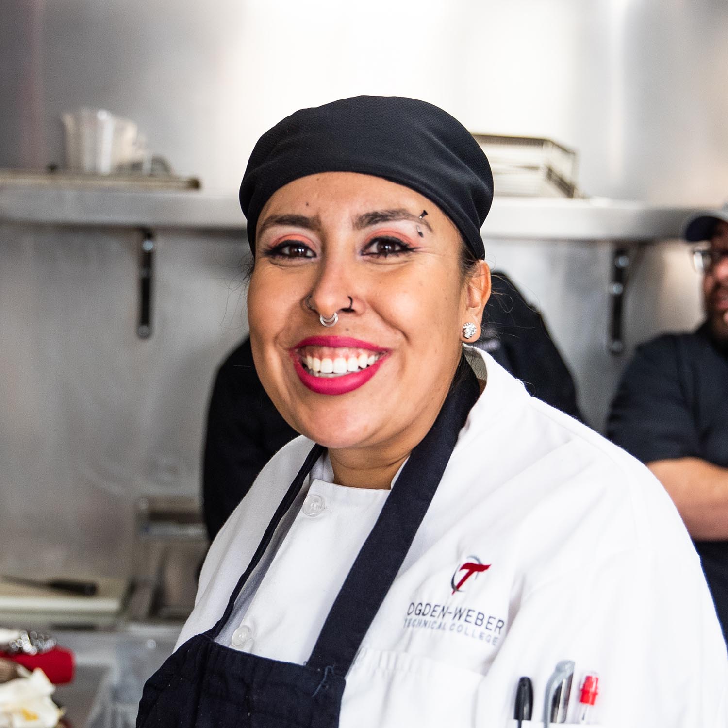 Woman in white chef's apron with logo and name 'Rosa' smiling at the camera.