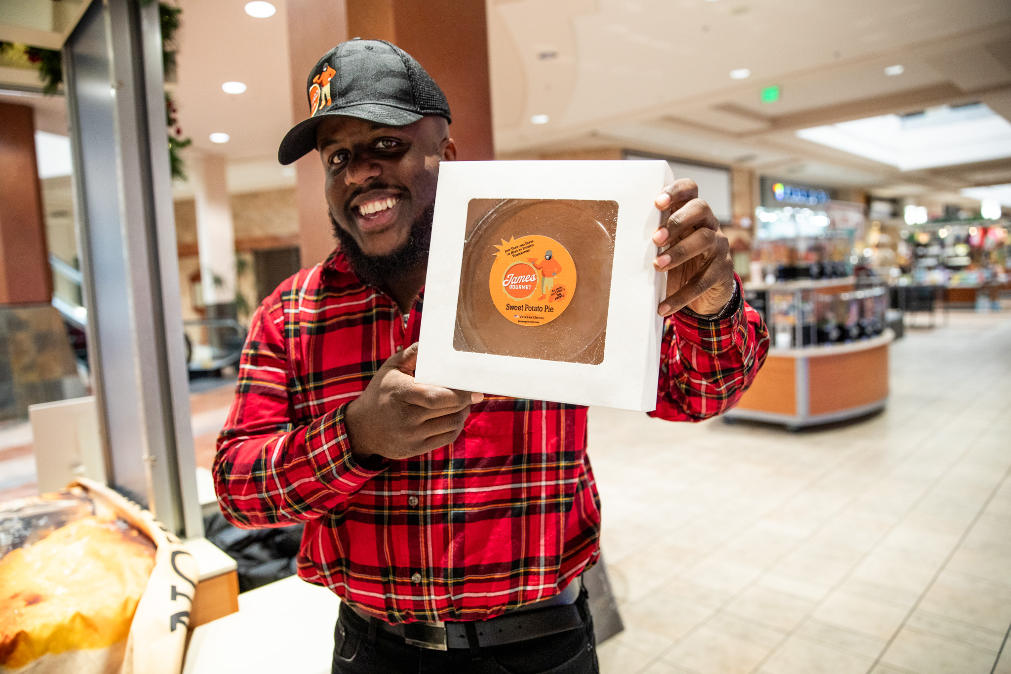 James Edwards smiling and holding up his James Gourmet Sweet Potato Pie product in a mall setting
