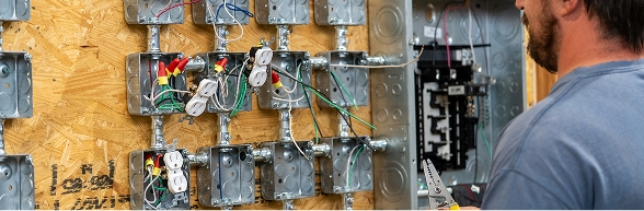 A man working with electrical panels and wiring mounted on a training board, representing OTECH's alumni association training programs for workforce development and continuing education