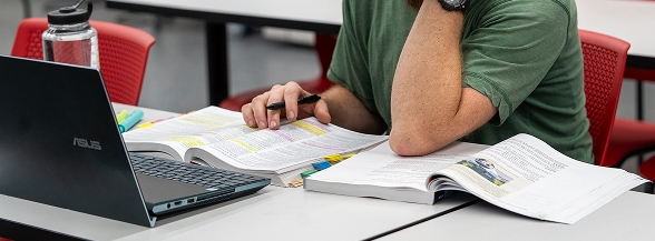 A student studying at a desk with a laptop and open textbooks in a classroom, representing the continuing education short courses and certificate programs available through OTECH for career upskilling
