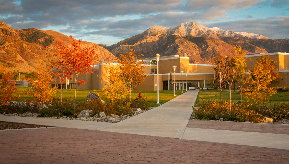 Aerial view of the Ogden-Weber Technical College campus building with colorful autumn trees lining a walkway and snow-capped mountains in the background, welcoming community members to OTECH's programs and services