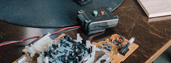 Electronic circuit boards and a small control device with green and red indicator lights displayed on a wooden surface, representing the hands-on technology projects available at OTECH's summer camps for students