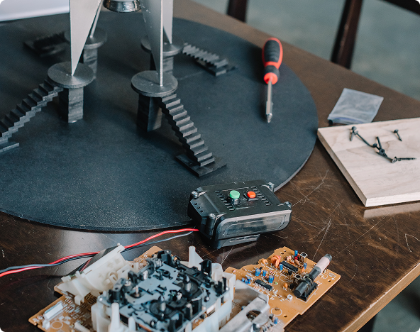 Electronic components including circuit boards, a gear-driven platform, and a screwdriver laid out on a table for hands-on robotics or electronics assembly at an OTECH summer camp