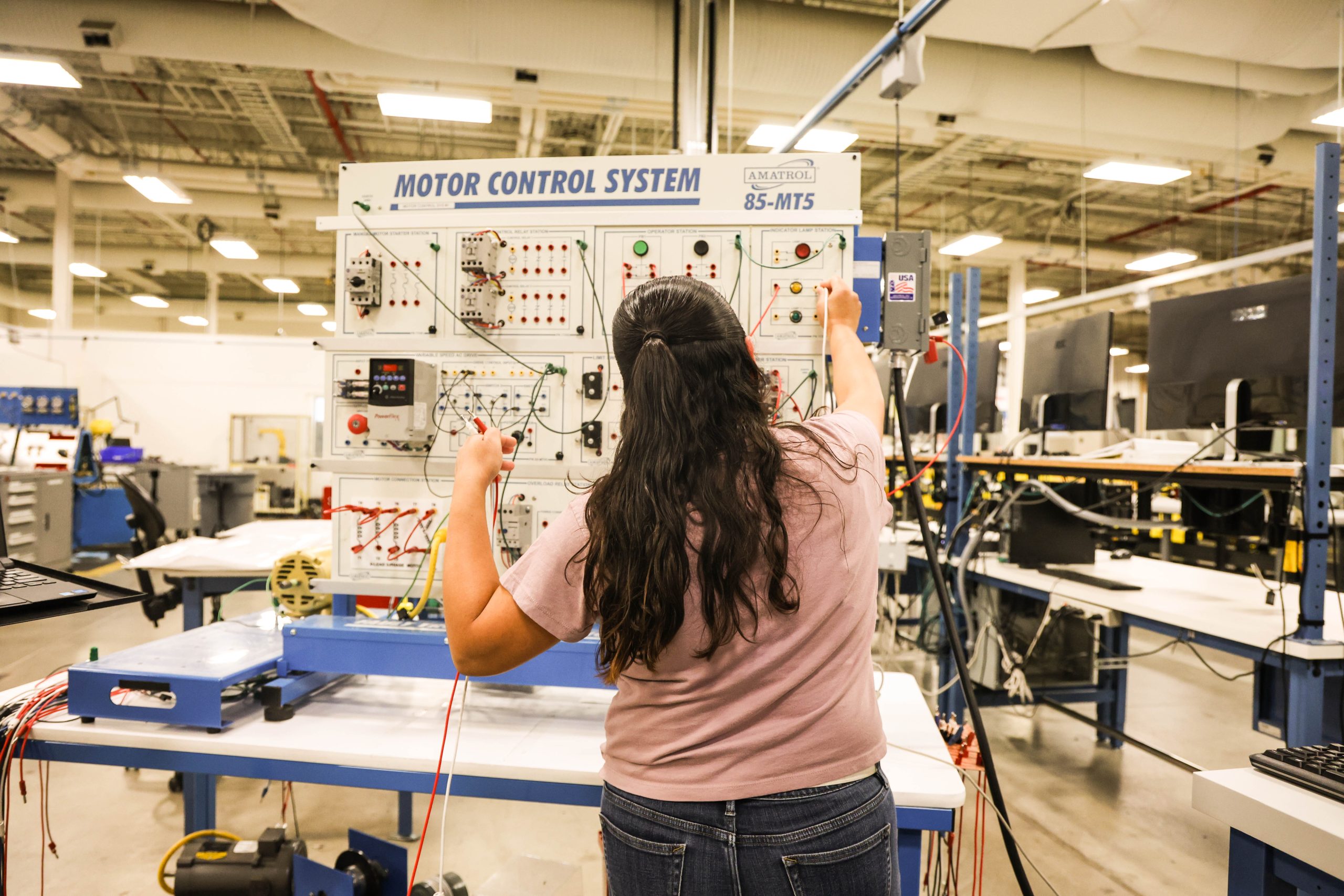 - Ogden Weber Technical College Student working with automation technology equipment, holding a wire inside the manufacturing building at Ogden-Weber Technical College.