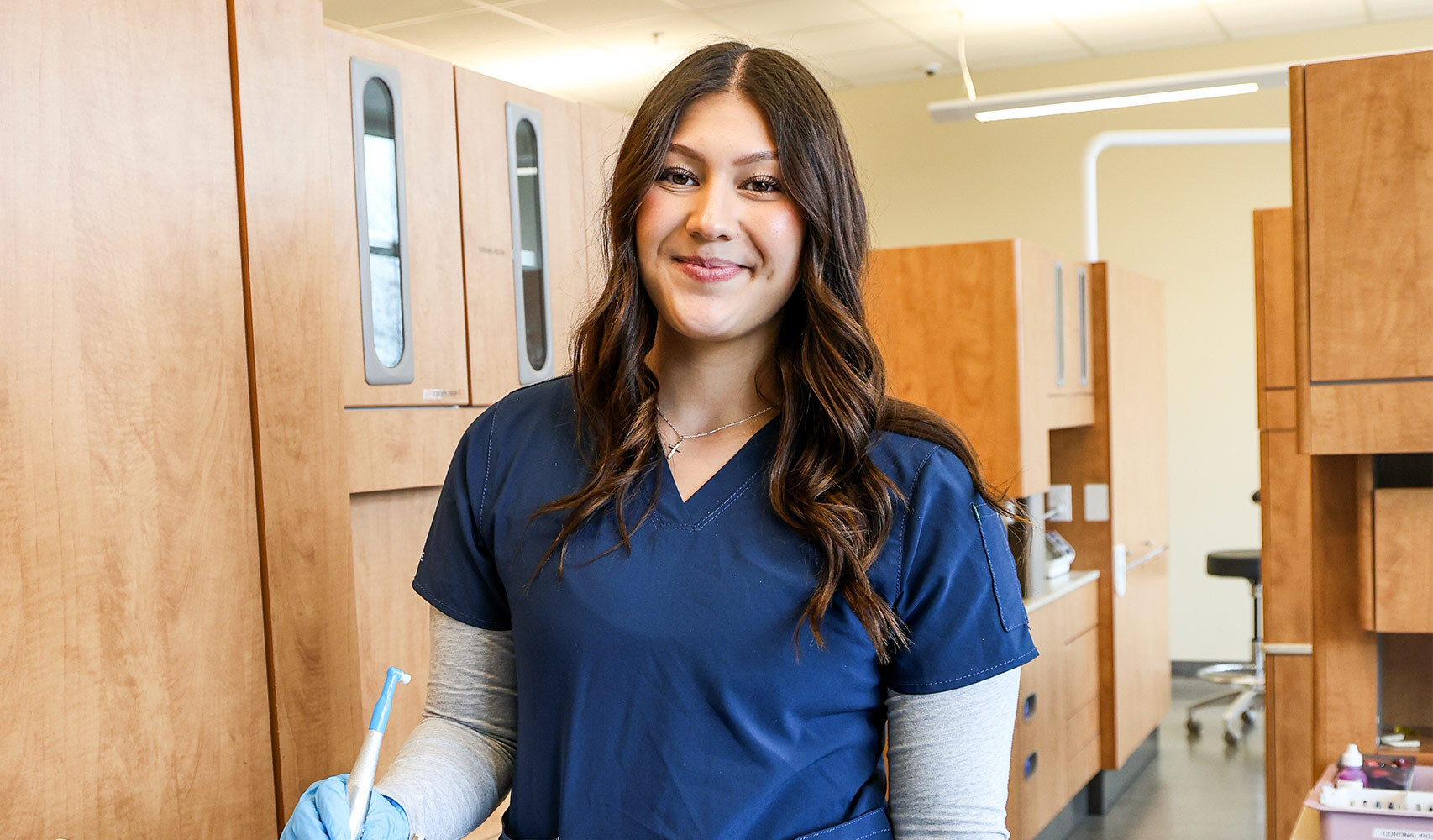 Woman in blue scrubs holding toothbrush and cup in a room.