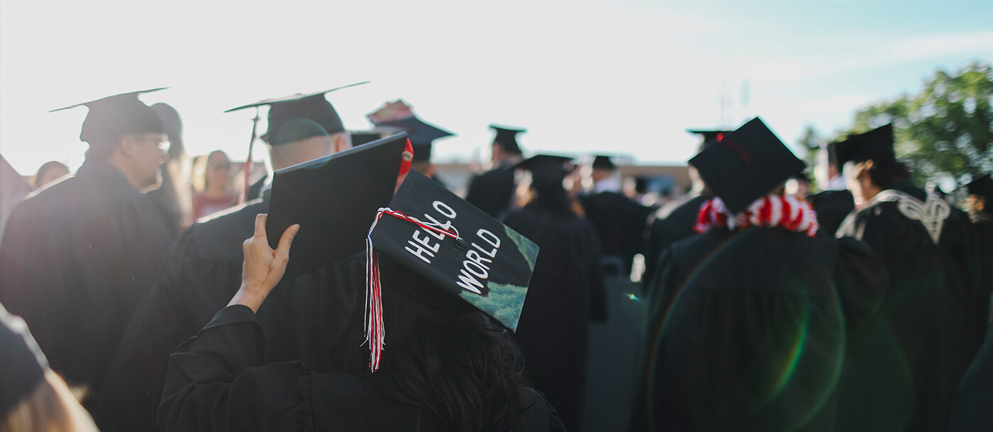 Graduates in black caps and gowns gathered outdoors.