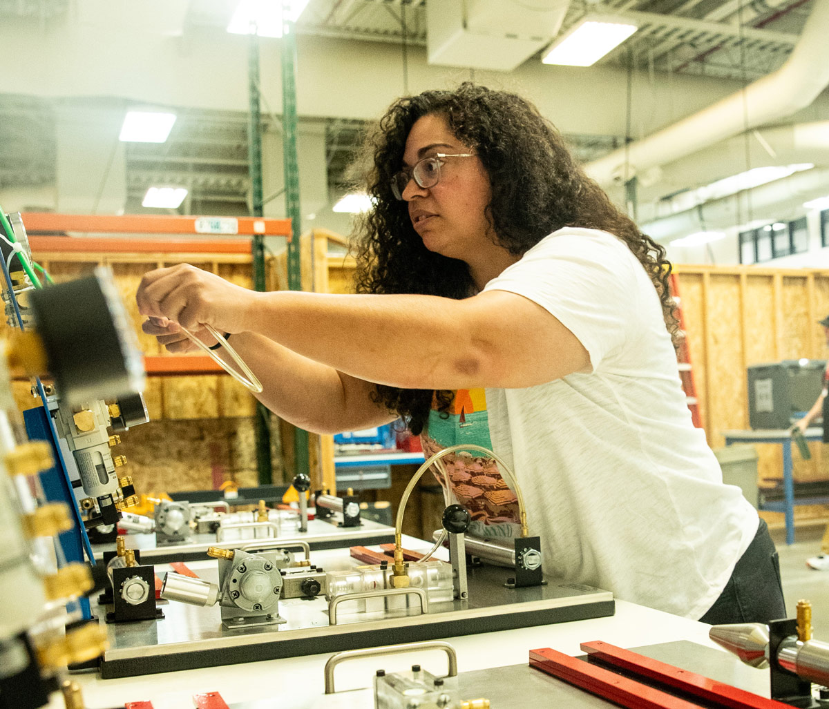 A female student with curly hair and glasses working at a fluid power and mechanical assembly training station in OTECH's Manufacturing Technology department