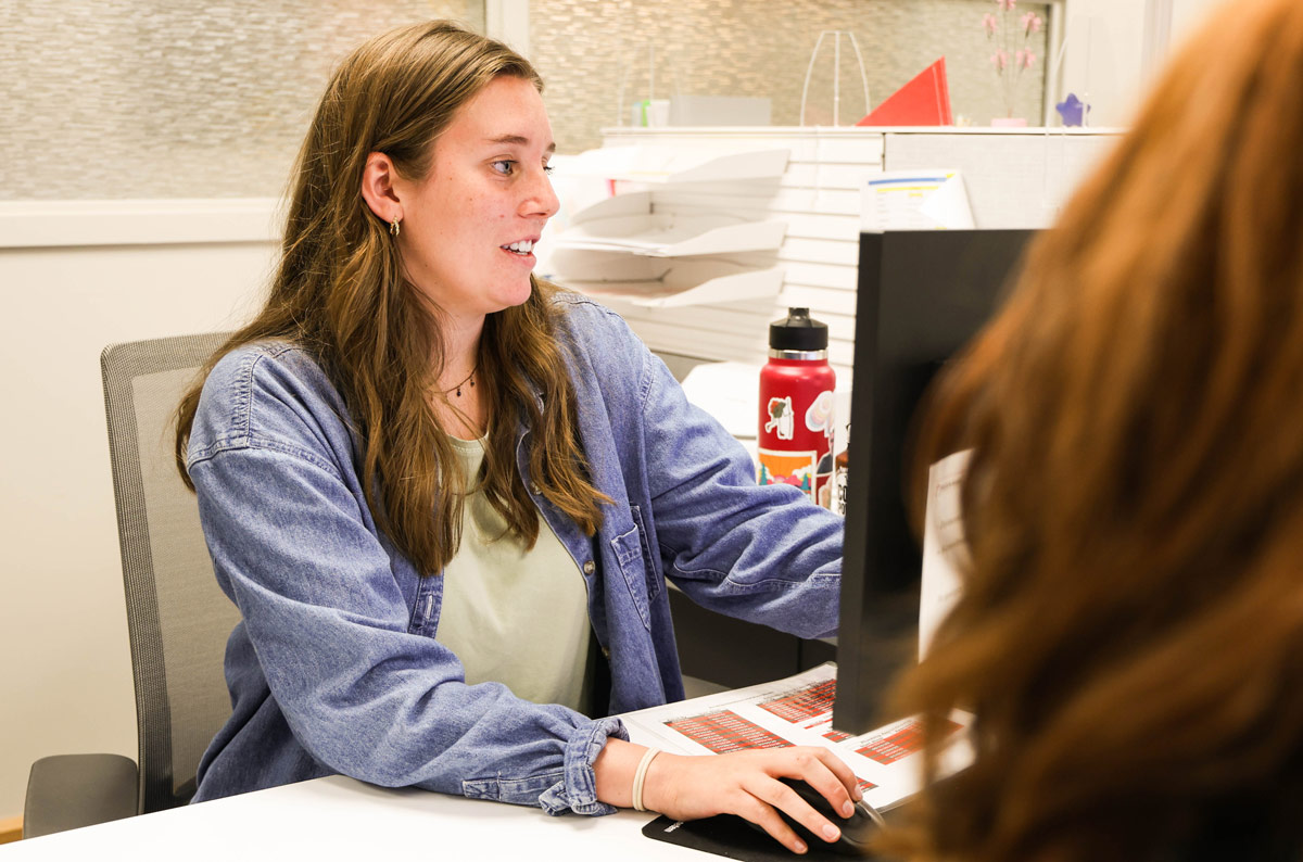 A prospective student in a denim jacket meets with an OTECH admissions advisor at a desk, getting help completing her application to enroll in a career training program