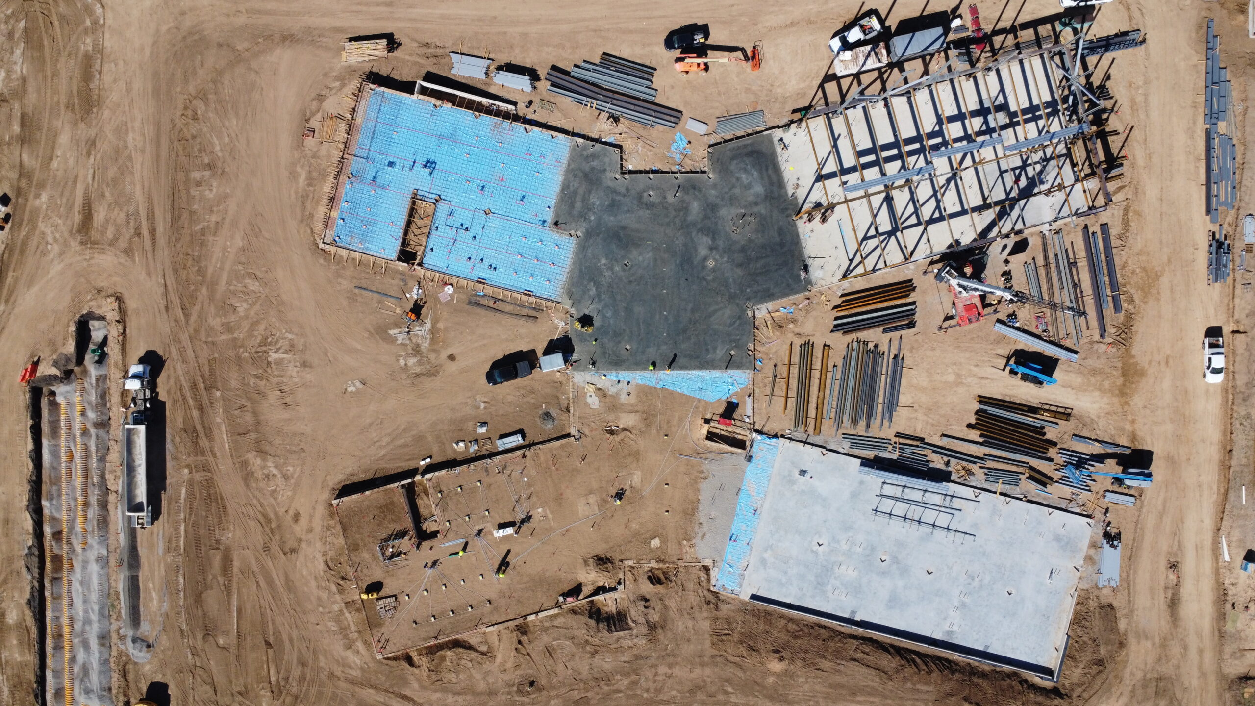 Aerial view of the Wasatch Peaks Pathway Building construction site in October 2026, showing concrete foundations, blue foundation insulation, and structural steel framing.