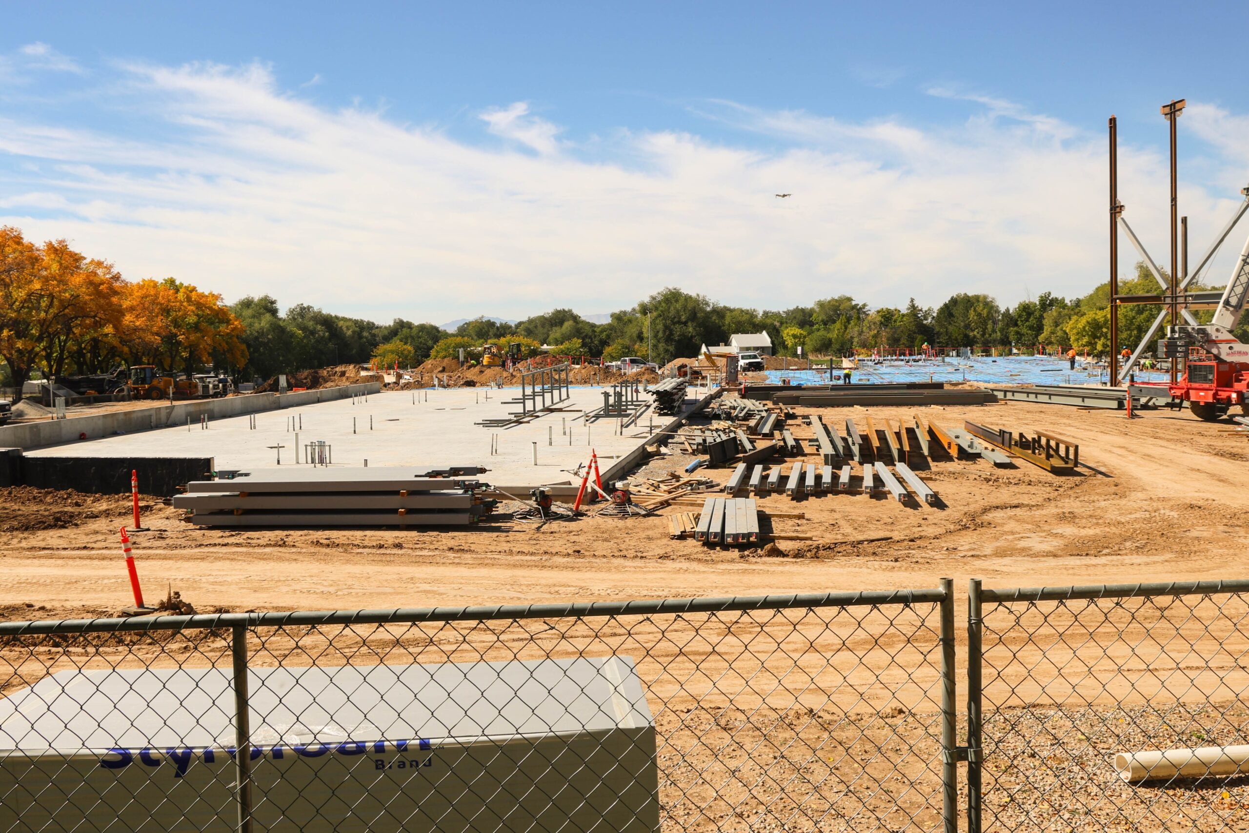 October construction progress on the new building, with a crane at the site and multiple steel columns and horizontal beams erected above the concrete foundation.
